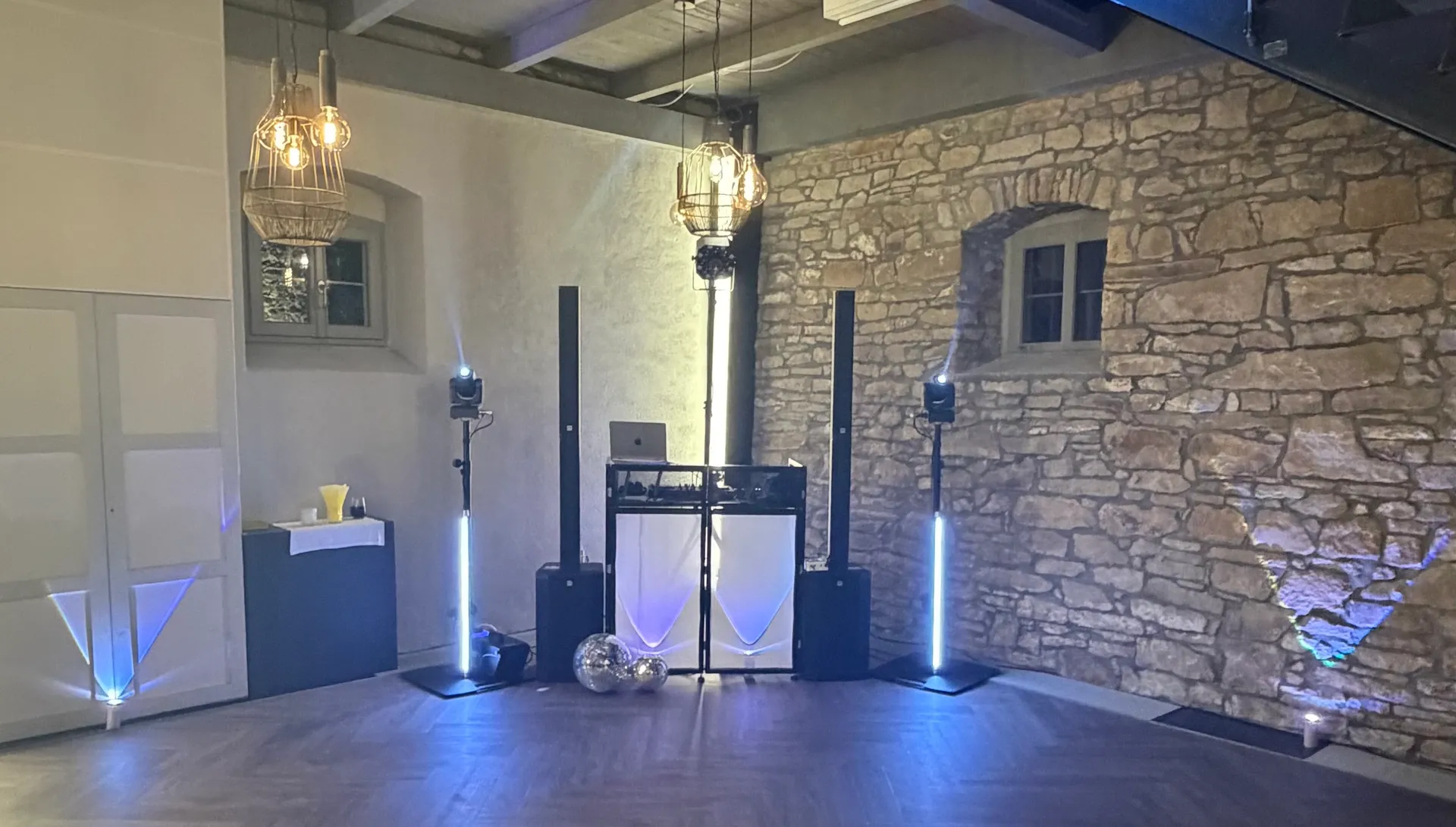 DJ-Setup von DJ Dan May bei einer Hochzeit in einer rustikalen Location in Franken – Booth, Säulen-Lautsprecher, LED-Lichtsäulen und Moving Heads vor Bruchsteinwand